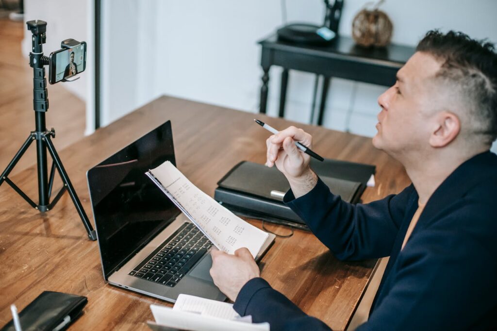 Educator engaged in an online class using a laptop and mobile device setup.